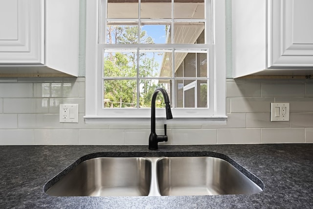 room details with backsplash, white cabinets, a sink, and dark stone countertops