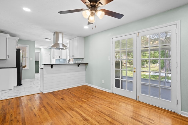 kitchen with wall chimney exhaust hood, freestanding refrigerator, white cabinetry, a ceiling fan, and a peninsula