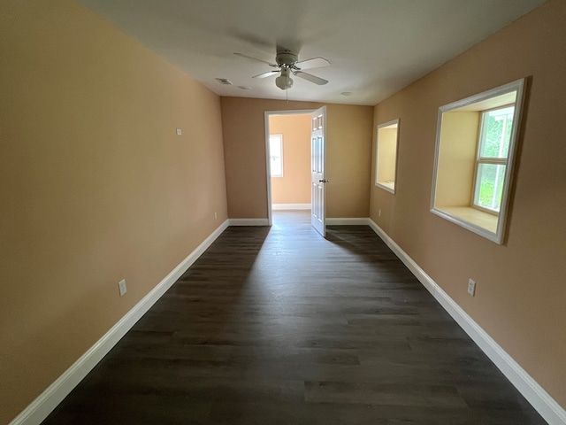 spare room featuring dark wood-style floors, a healthy amount of sunlight, baseboards, and a ceiling fan