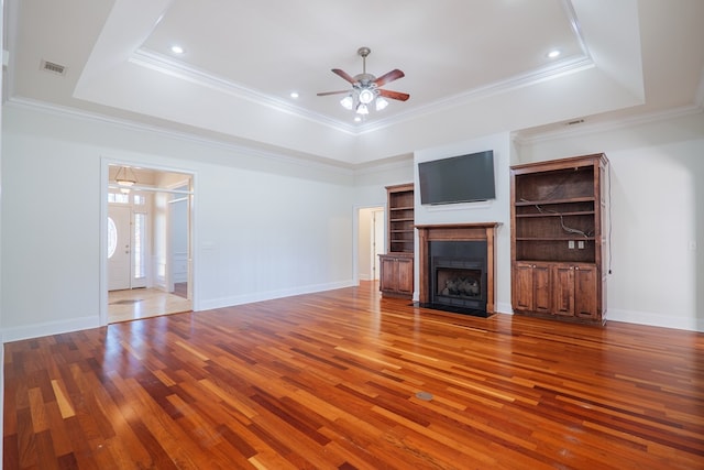 unfurnished living room with hardwood / wood-style flooring, ceiling fan, ornamental molding, and a tray ceiling