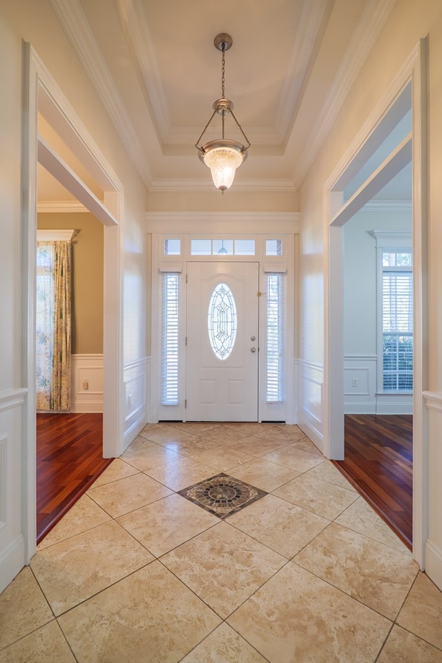 foyer with light hardwood / wood-style floors, a tray ceiling, and ornamental molding