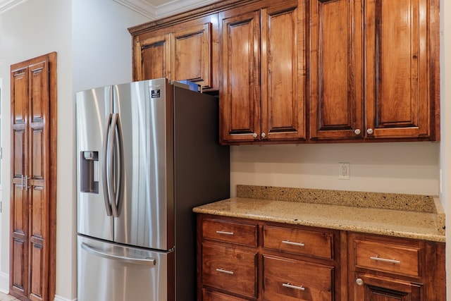 kitchen with light stone countertops, stainless steel refrigerator with ice dispenser, and ornamental molding