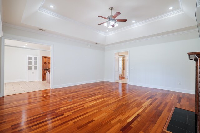 spare room with a tray ceiling, ceiling fan, ornamental molding, and light wood-type flooring