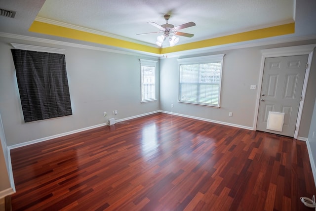 empty room with a raised ceiling, ornamental molding, and dark hardwood / wood-style flooring