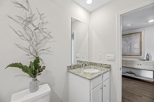 half bathroom featuring recessed lighting, vanity, toilet, and wood finished floors