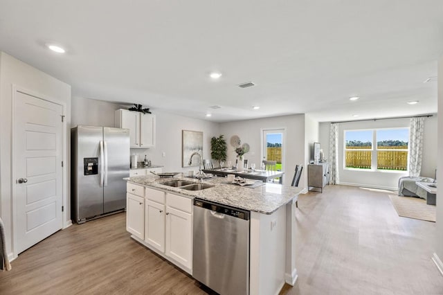 kitchen with light wood-style flooring, appliances with stainless steel finishes, white cabinets, a sink, and an island with sink