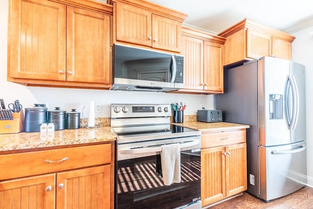 kitchen with light stone counters, ornamental molding, light hardwood / wood-style floors, and appliances with stainless steel finishes