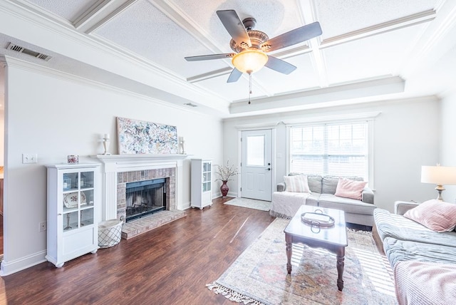 living room with ceiling fan, dark wood-type flooring, coffered ceiling, a brick fireplace, and ornamental molding