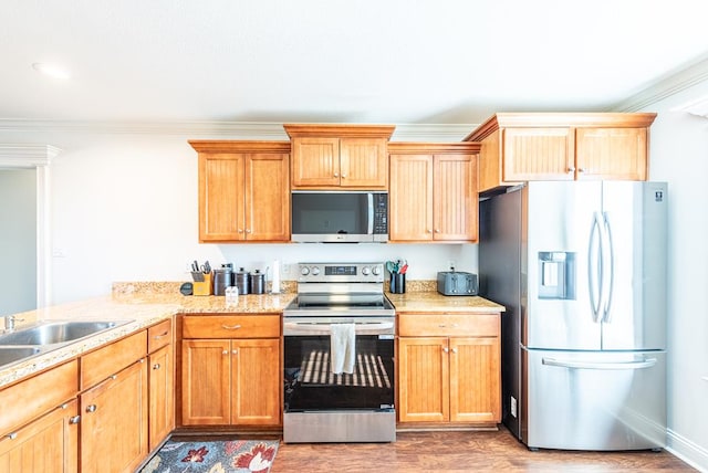 kitchen with appliances with stainless steel finishes, sink, ornamental molding, and hardwood / wood-style floors