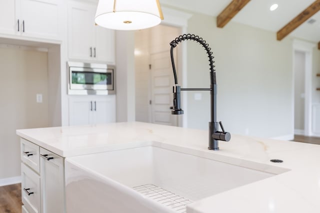 4856 Brown Cat Cir, Hahira, GA 31632 - kitchen with stainless steel microwave, beamed ceiling, light stone countertops, white cabinets, and wood finished floors