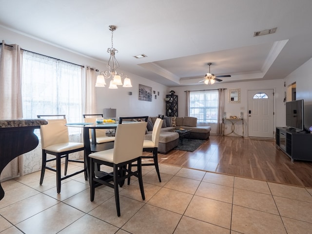 tiled dining area with ornamental molding, ceiling fan with notable chandelier, and a tray ceiling