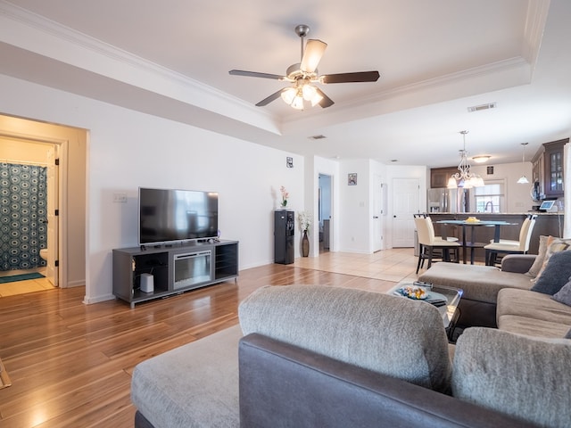 living room with a raised ceiling, crown molding, ceiling fan with notable chandelier, and light hardwood / wood-style floors