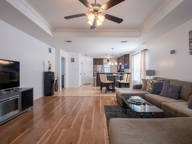 living room with ceiling fan with notable chandelier, ornamental molding, light hardwood / wood-style floors, and a raised ceiling