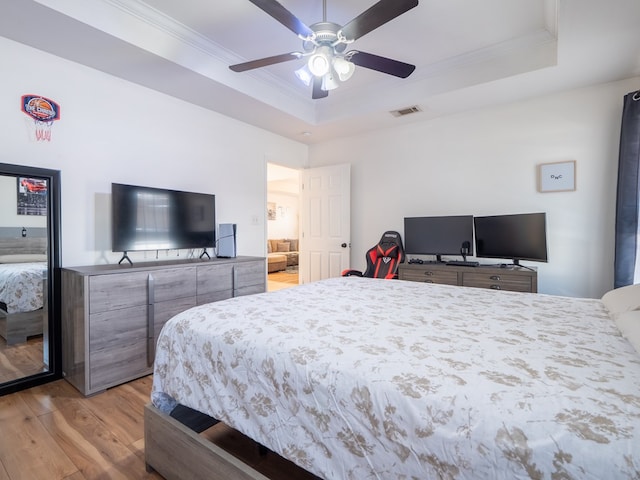 bedroom with a tray ceiling, ornamental molding, light hardwood / wood-style floors, and ceiling fan