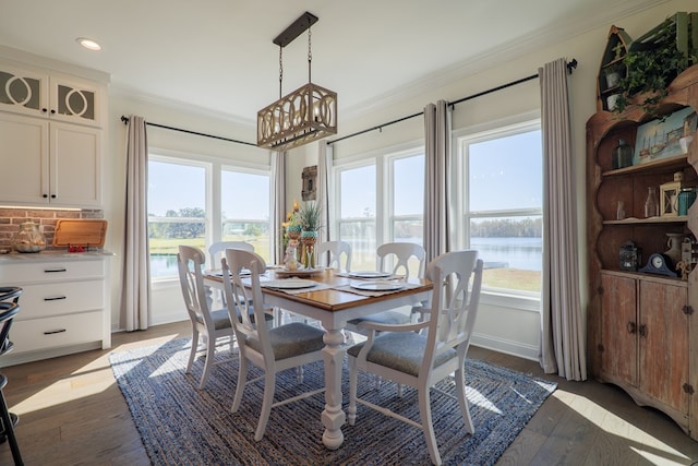 dining room with a water view, ornamental molding, dark wood-type flooring, and a chandelier