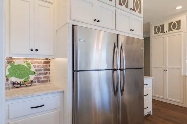 kitchen featuring white cabinetry, light stone countertops, dark hardwood / wood-style flooring, stainless steel fridge, and decorative backsplash