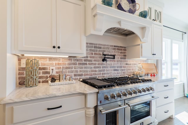 kitchen with decorative backsplash, range with two ovens, white cabinetry, and light stone counters