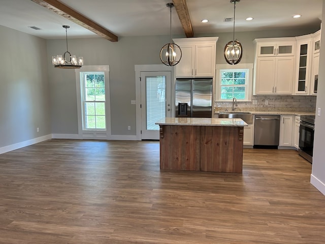 kitchen with beam ceiling, stainless steel appliances, white cabinetry, and a healthy amount of sunlight