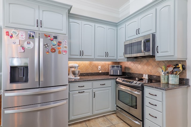 kitchen with decorative backsplash, appliances with stainless steel finishes, dark stone counters, ornamental molding, and light tile patterned floors