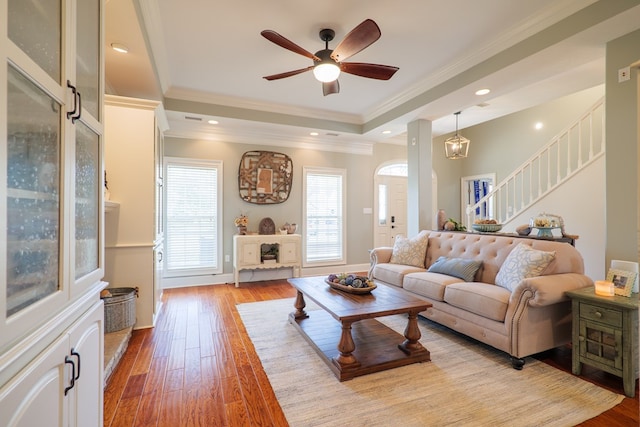 living room with light wood-type flooring, a tray ceiling, ceiling fan, and crown molding