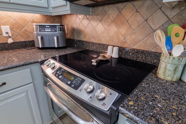 kitchen featuring stainless steel electric range, white cabinetry, backsplash, and dark stone counters