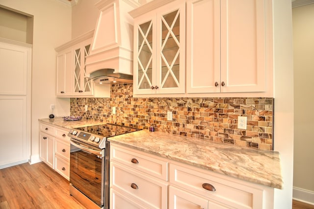 kitchen with decorative backsplash, light stone counters, electric stove, white cabinets, and light hardwood / wood-style floors