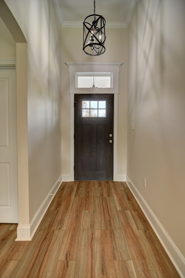 entrance foyer featuring an inviting chandelier, ornamental molding, and light wood-type flooring