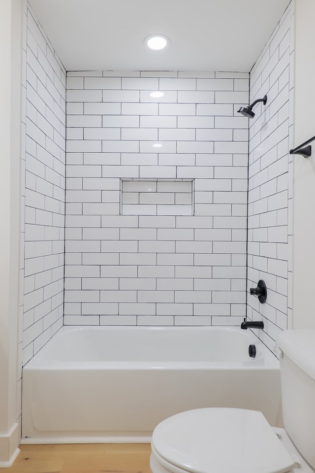 bathroom with wood-type flooring, toilet, and tiled shower / bath