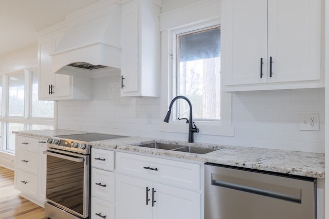 kitchen featuring sink, custom exhaust hood, stainless steel appliances, light stone countertops, and white cabinets