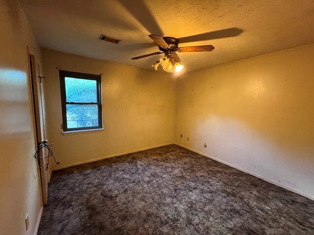 empty room with ceiling fan, dark carpet, and a textured ceiling