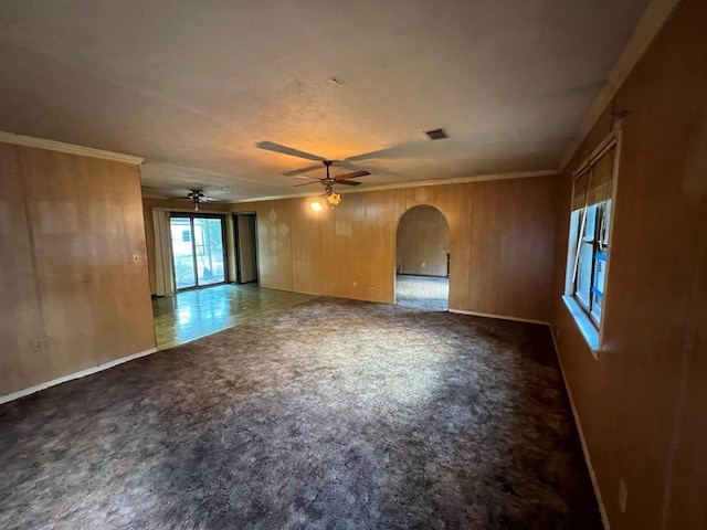 spare room featuring ceiling fan, ornamental molding, and wood walls