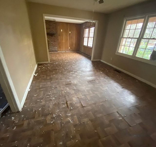 empty room with wood walls, plenty of natural light, and ceiling fan