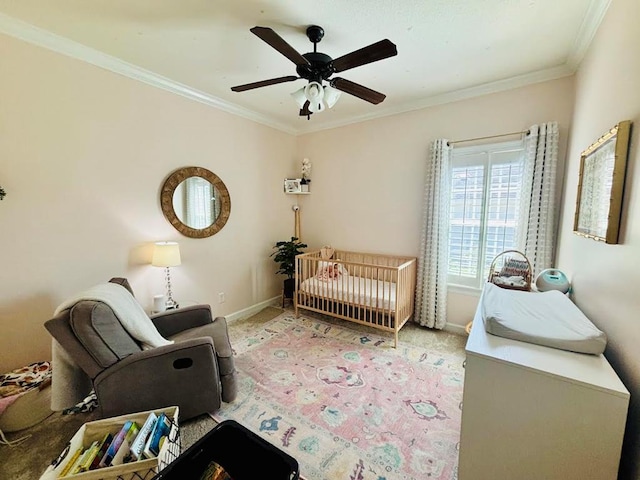 carpeted bedroom with a crib, a ceiling fan, baseboards, and ornamental molding