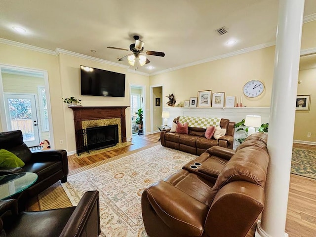 living area with a ceiling fan, wood finished floors, visible vents, a fireplace with flush hearth, and ornamental molding