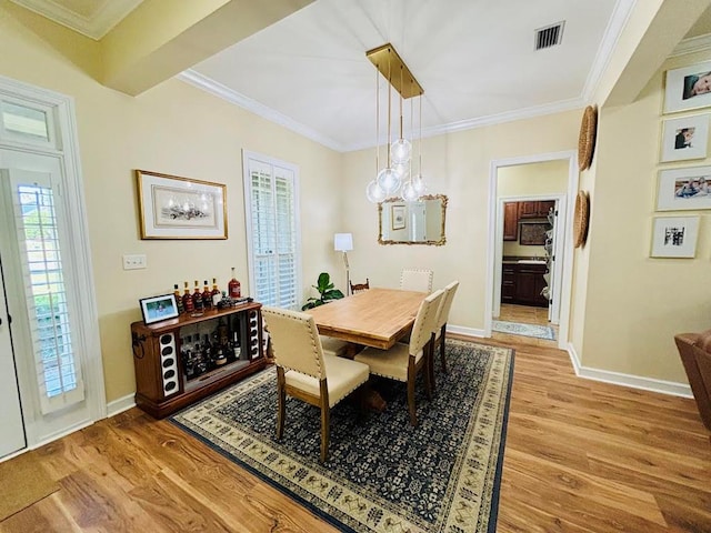 dining space with baseboards, visible vents, light wood finished floors, and ornamental molding