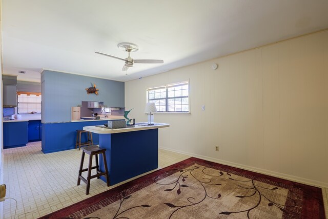 kitchen with ceiling fan, blue cabinets, a breakfast bar area, and a wealth of natural light