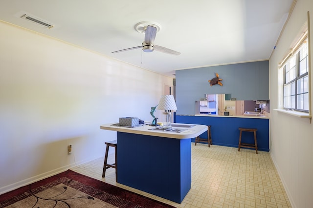 kitchen featuring kitchen peninsula, ceiling fan, a breakfast bar, and crown molding