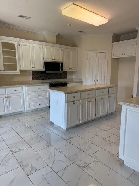 kitchen with stainless steel microwave, marble finish floor, crown molding, and visible vents