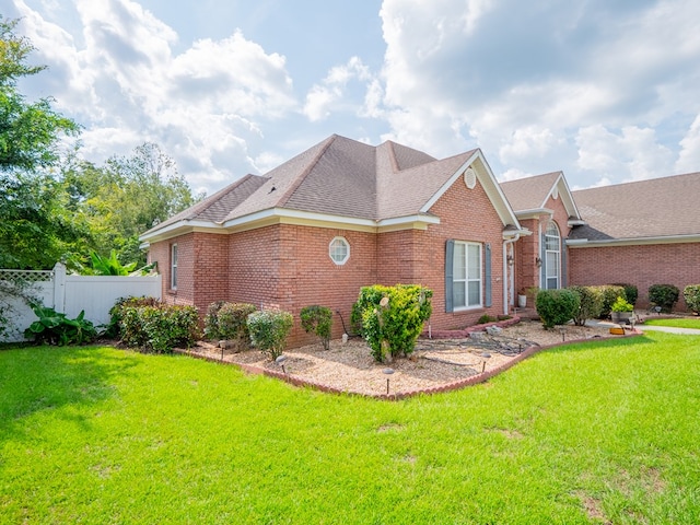 view of home's exterior with fence, a lawn, brick siding, and roof with shingles