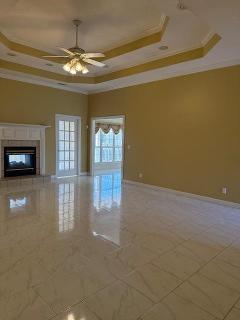 unfurnished living room featuring baseboards, ceiling fan, crown molding, a tiled fireplace, and a raised ceiling