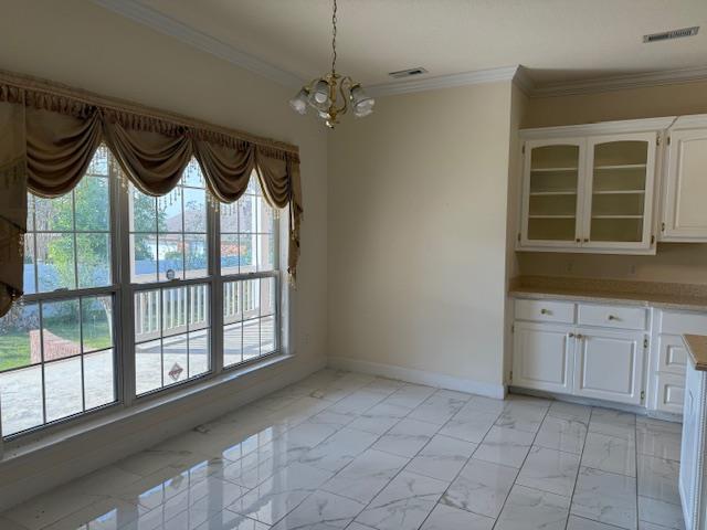 unfurnished dining area featuring visible vents, crown molding, baseboards, a chandelier, and marble finish floor