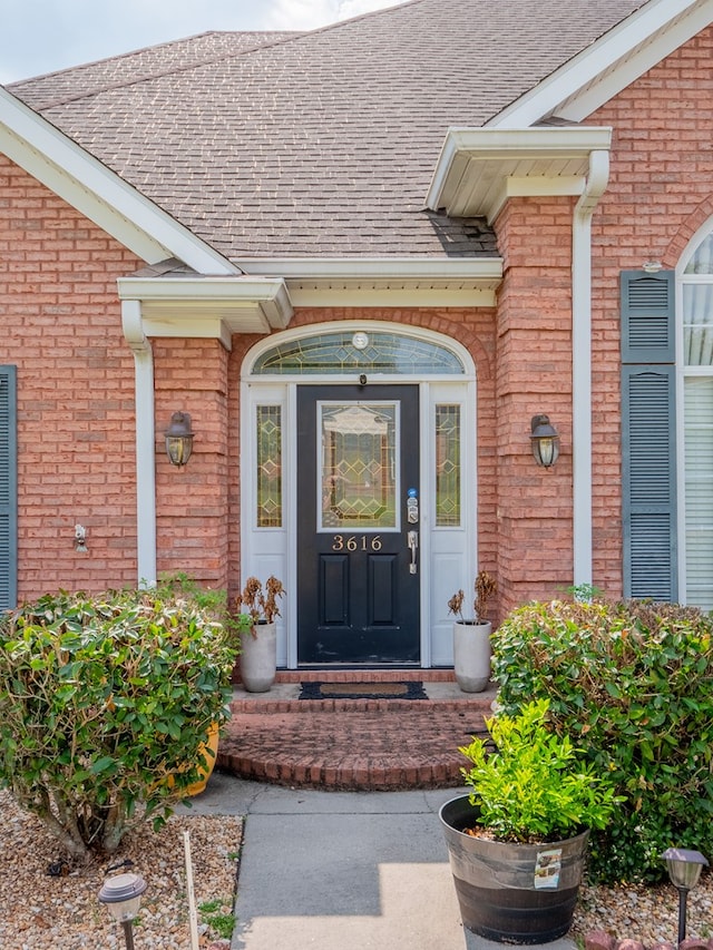 property entrance featuring brick siding and roof with shingles