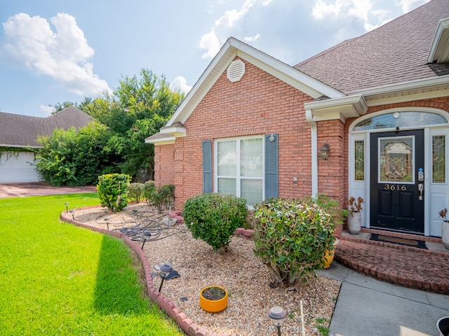 entrance to property featuring a yard, brick siding, and a shingled roof