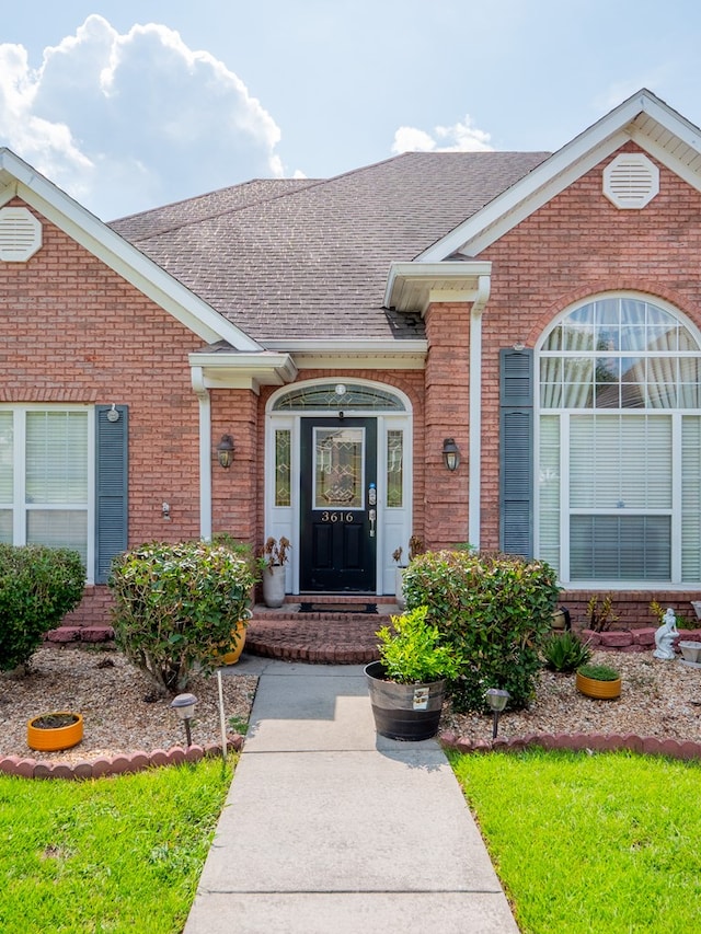 entrance to property with brick siding and a shingled roof