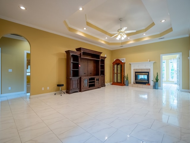 unfurnished living room featuring a tray ceiling, arched walkways, ornamental molding, and a tiled fireplace