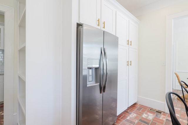 200 E College St, Valdosta, GA 31602 - kitchen with visible vents, baseboards, stainless steel fridge, brick floor, and white cabinets