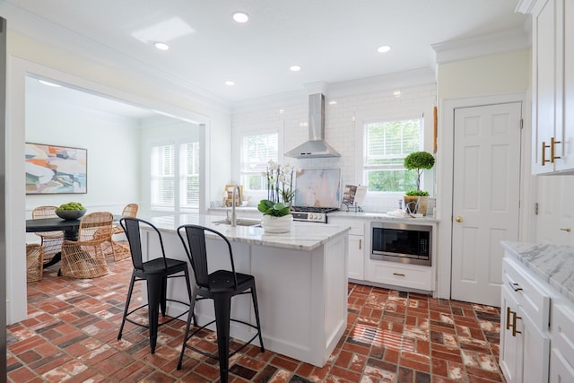 200 E College St, Valdosta, GA 31602 - kitchen featuring wall chimney range hood, crown molding, stainless steel microwave, and brick floor