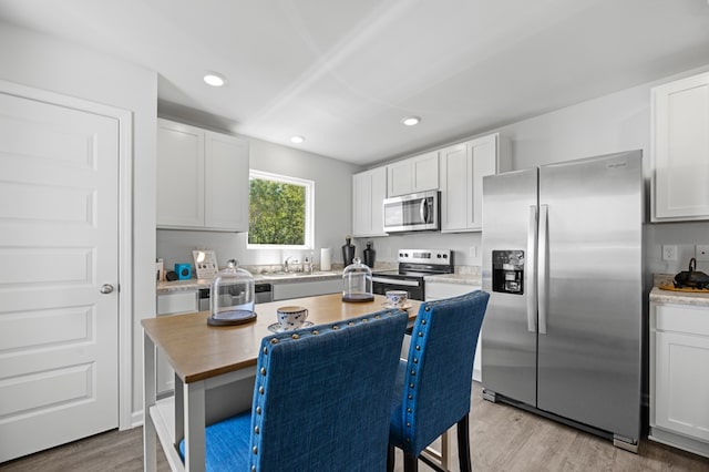 kitchen with light wood finished floors, stainless steel appliances, recessed lighting, white cabinetry, and a sink