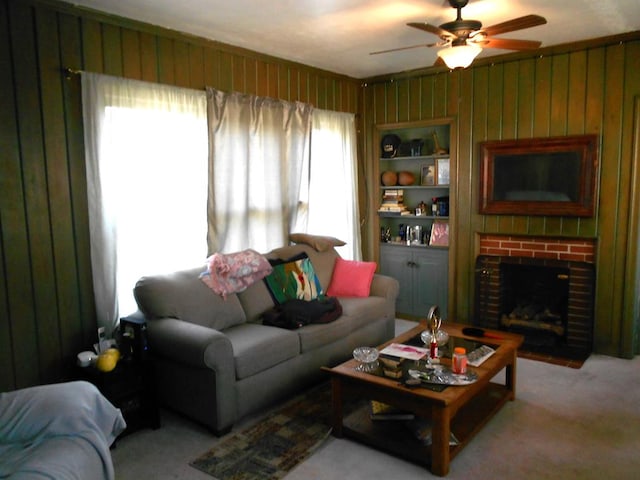 living room with a ceiling fan, a brick fireplace, light colored carpet, and wooden walls