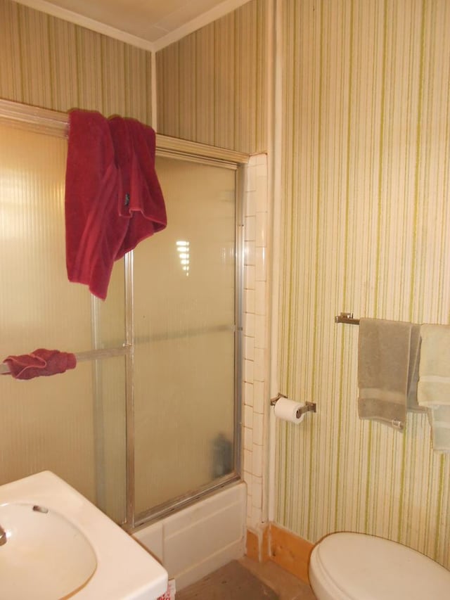 bathroom with toilet, wallpapered walls, and bath / shower combo with glass door